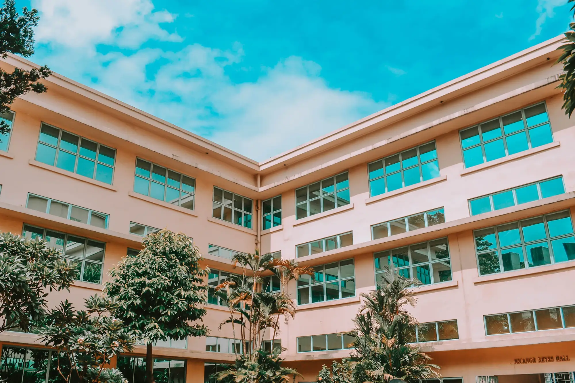 Pink and teal school building against a blue sky with trees