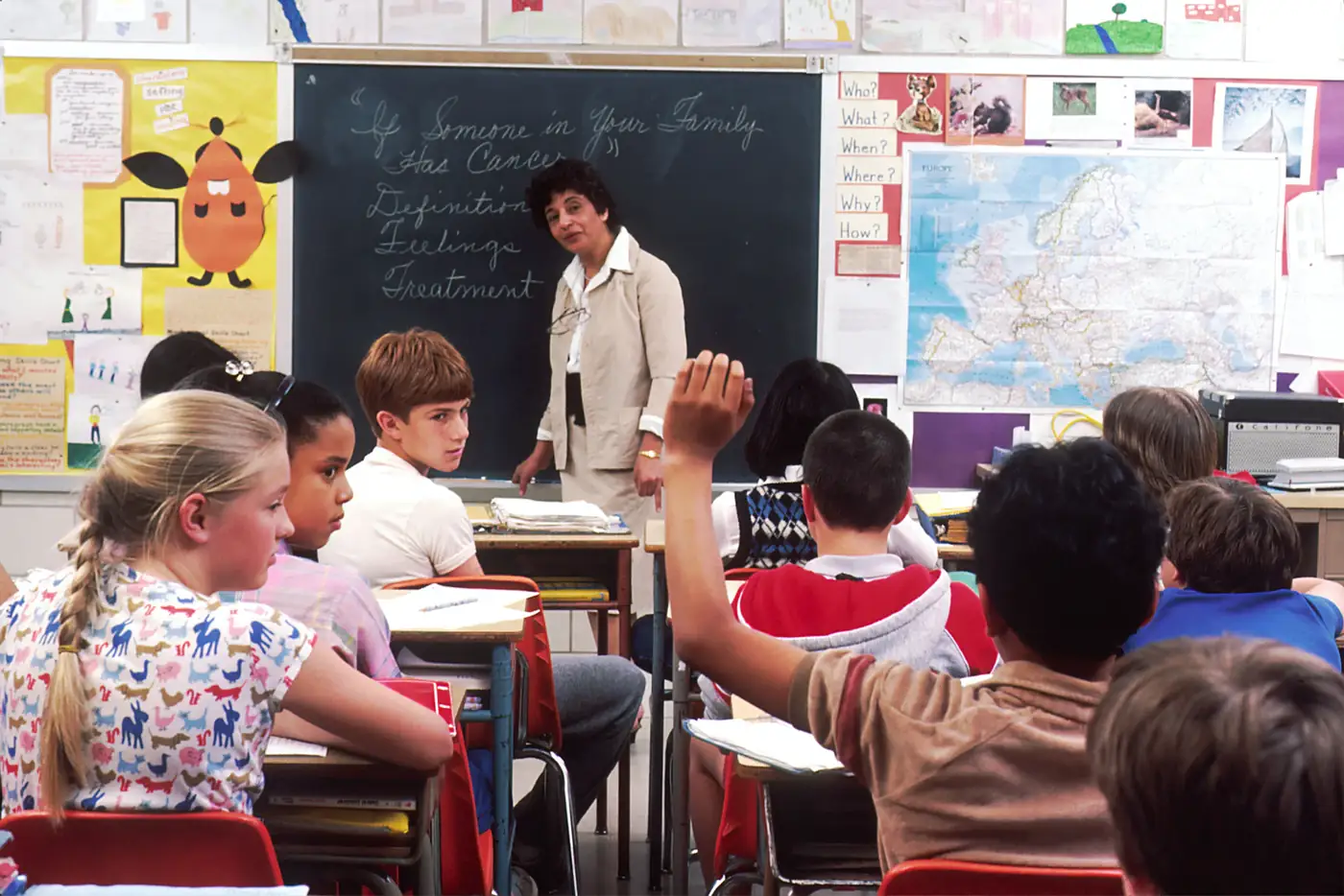 A teacher in a classroom with children raising their hands
