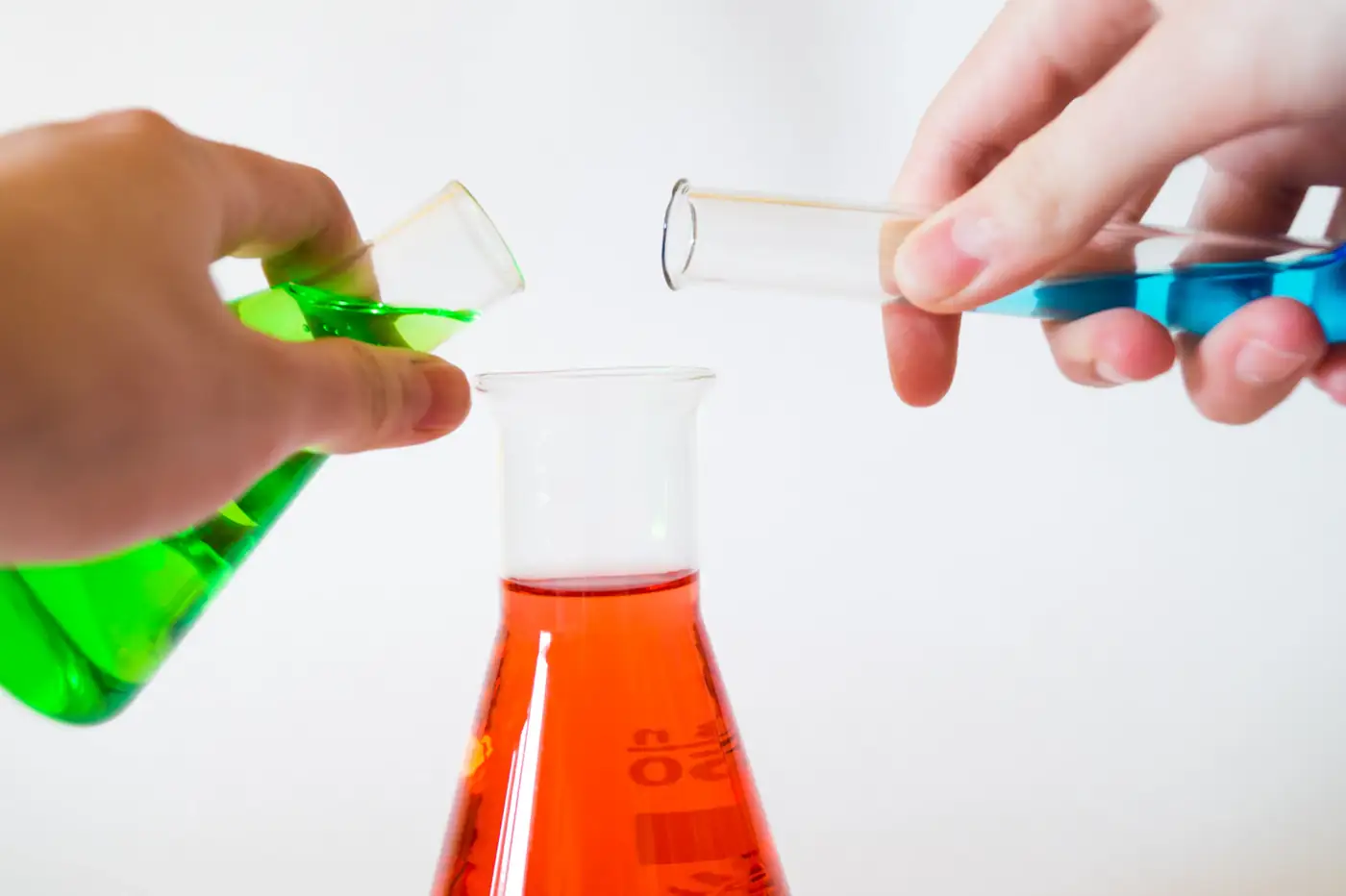 Hands pouring liquid between test tubes beside a red flask