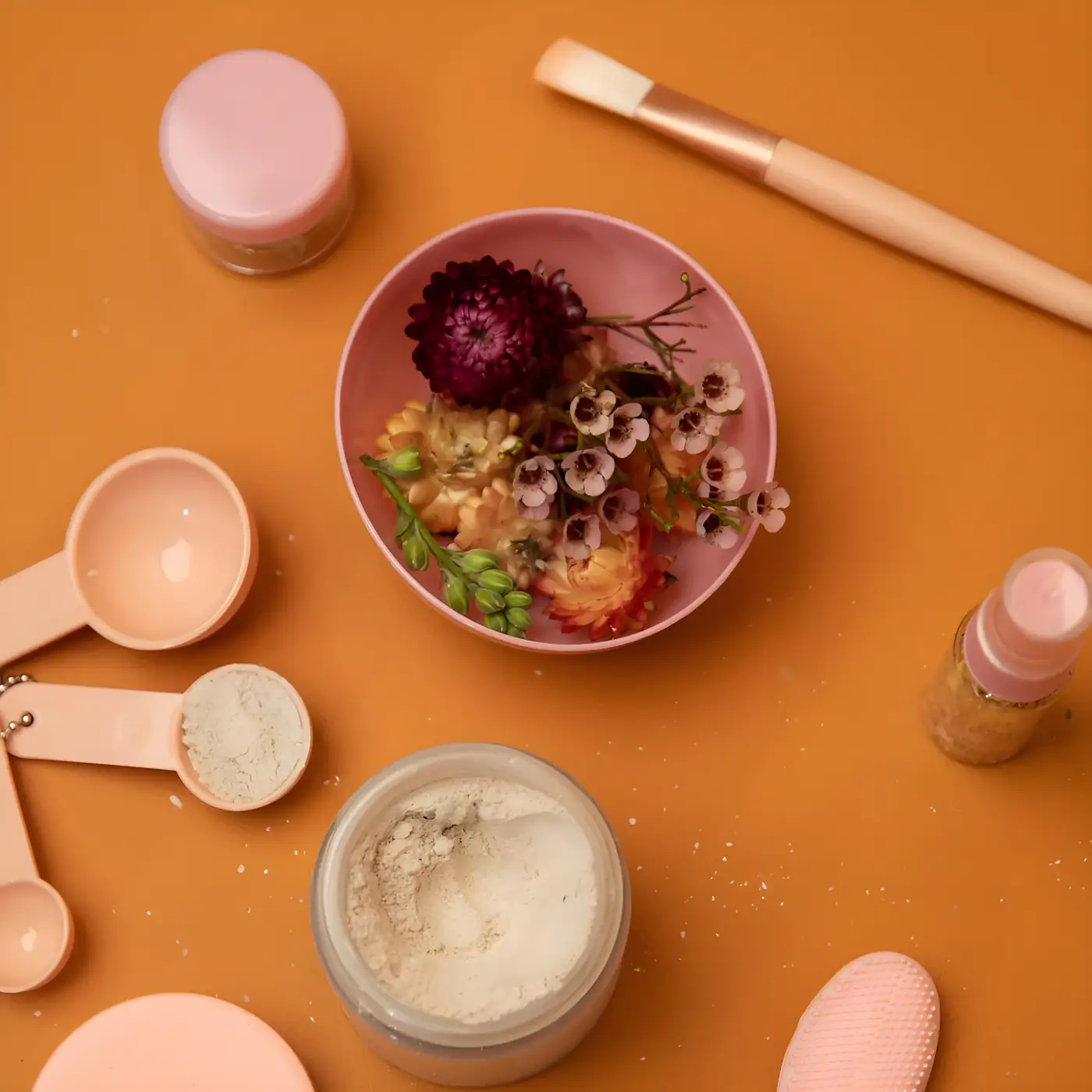 Bowl of dried flowers with a cream jar and brush on orange