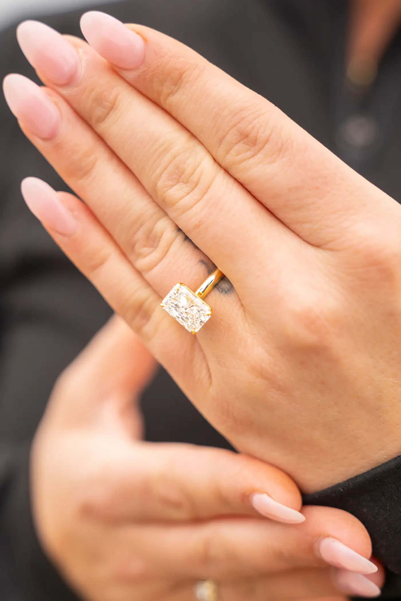 Hand wearing an emerald cut diamond ring in warm light
