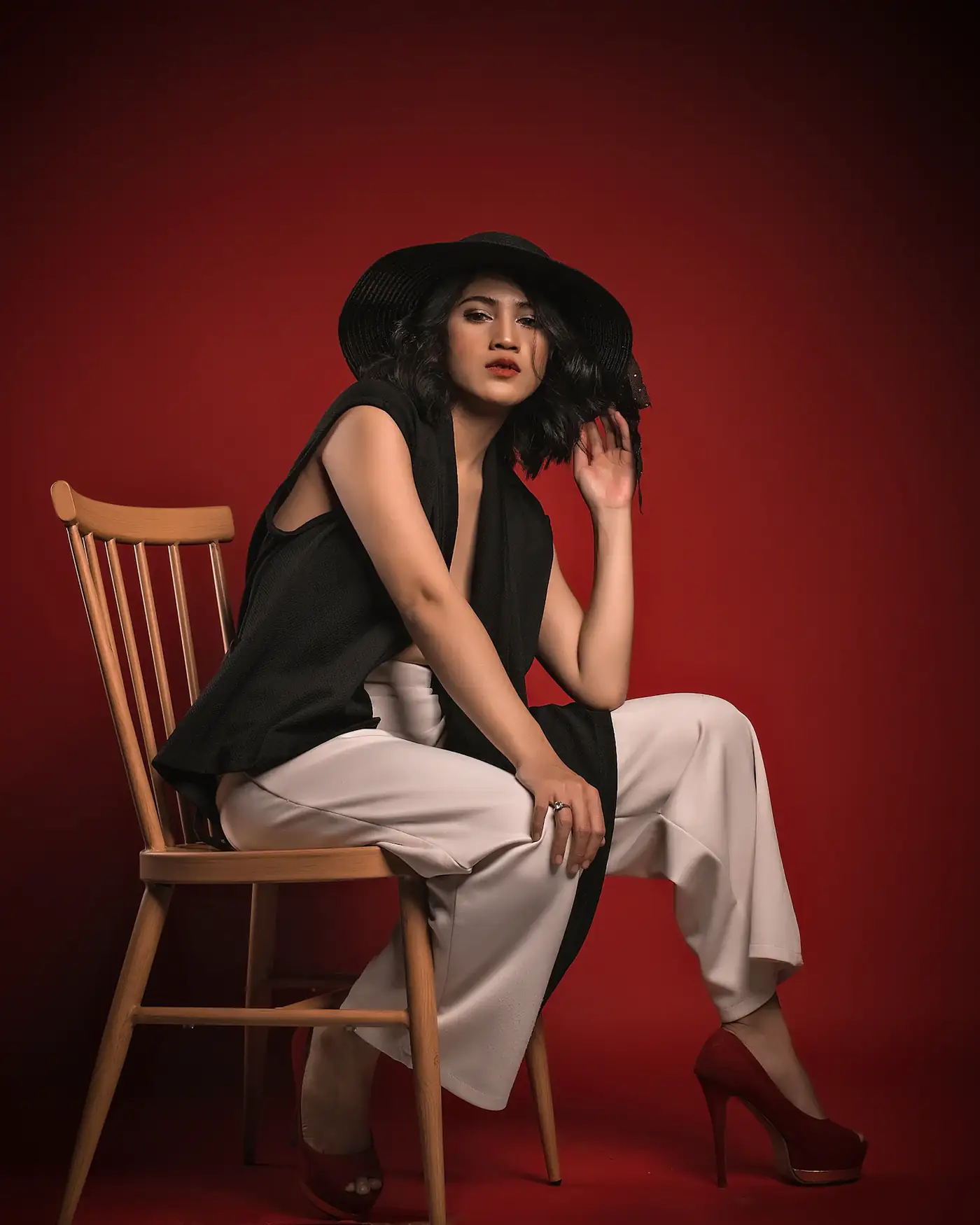 Model seated on a wooden chair against a red wall
