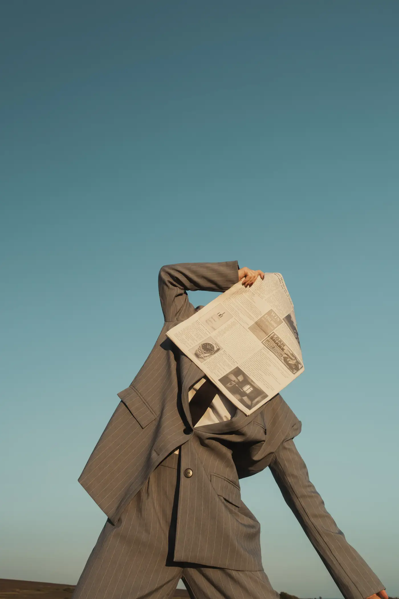 Model holding a newspaper in a brown coat against teal