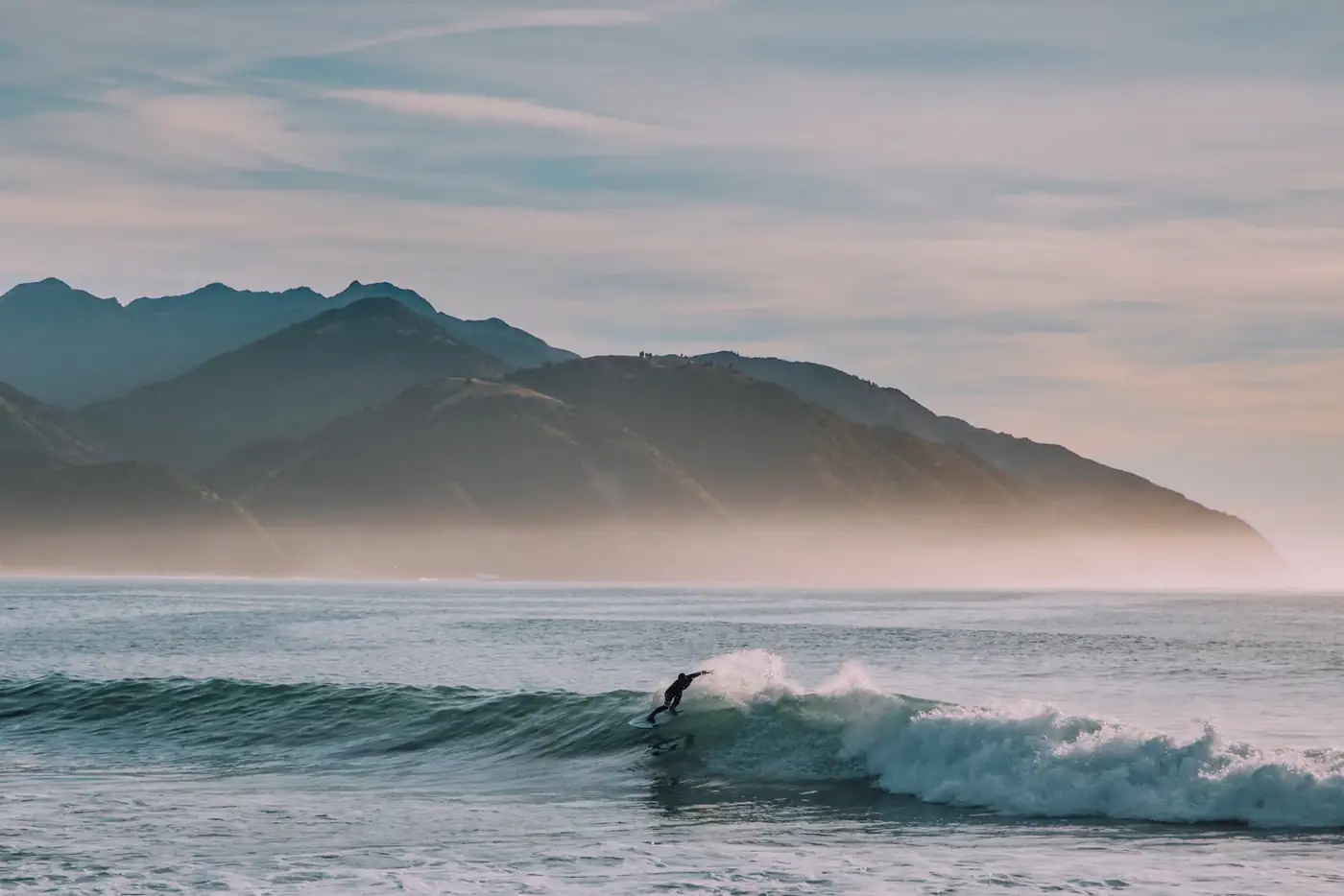 Lone surfer below misty mountains