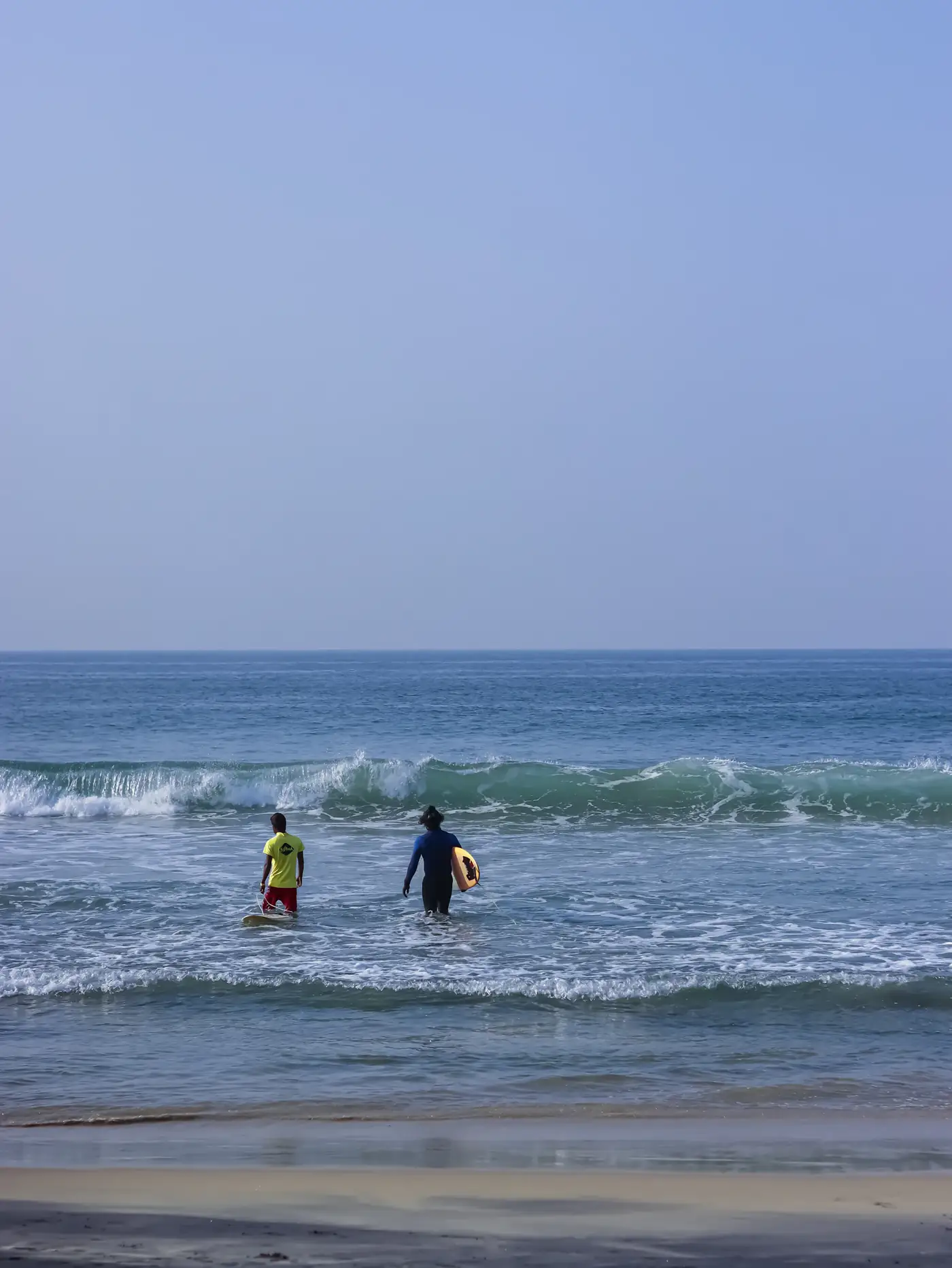 Two beginners walking into the white water with boards