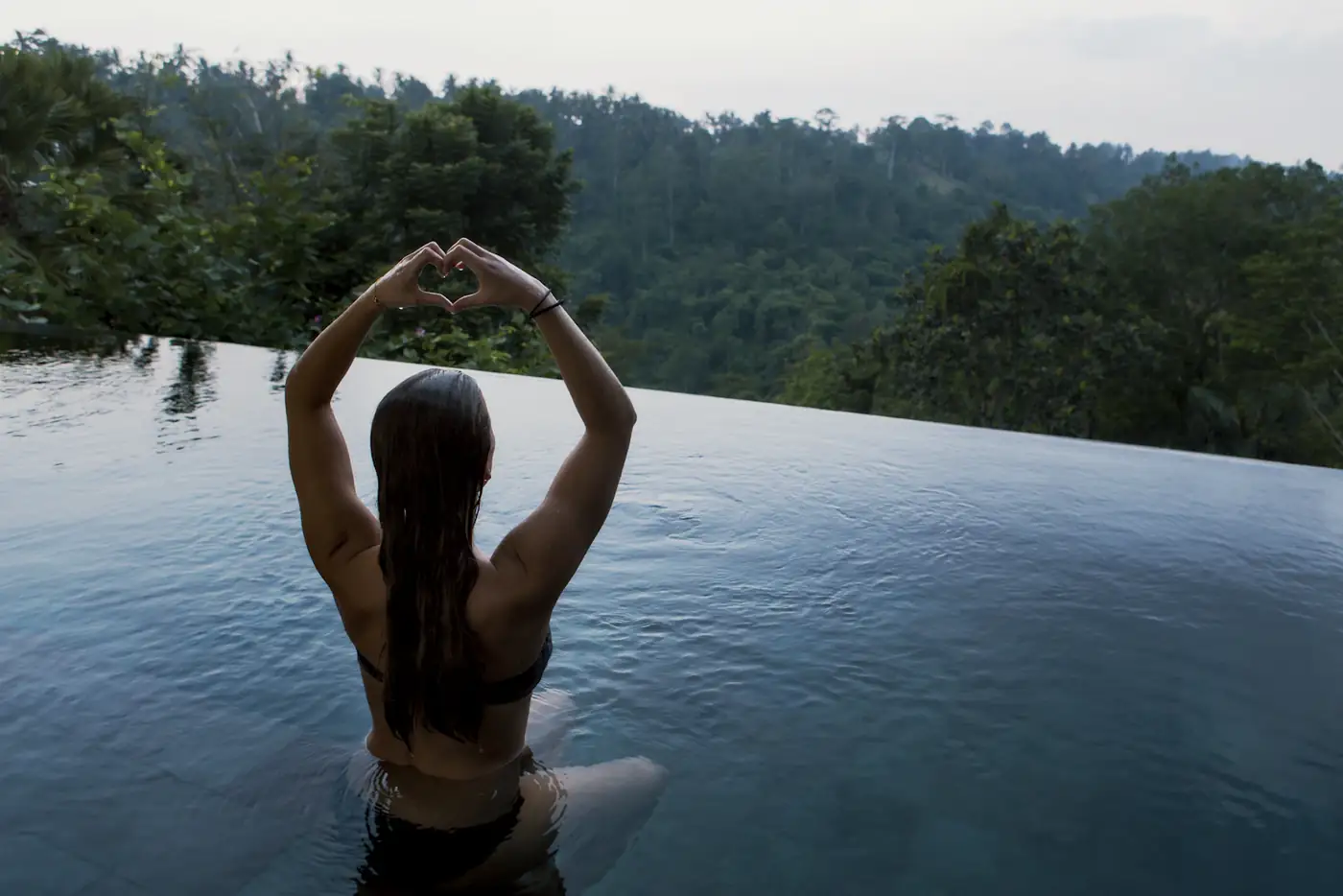 Woman in an infinity pool facing forested hills