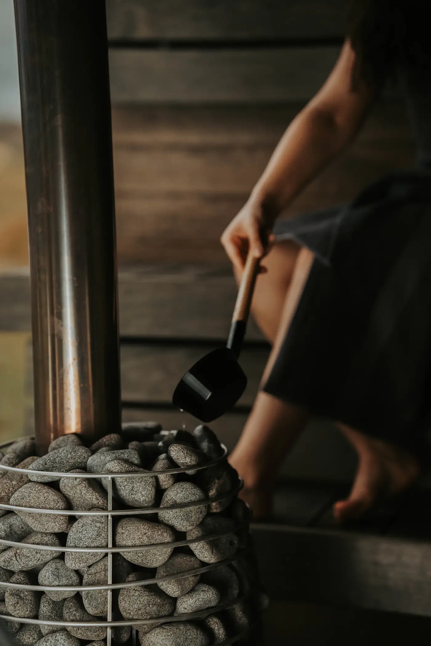 Hand pouring water over hot sauna stones