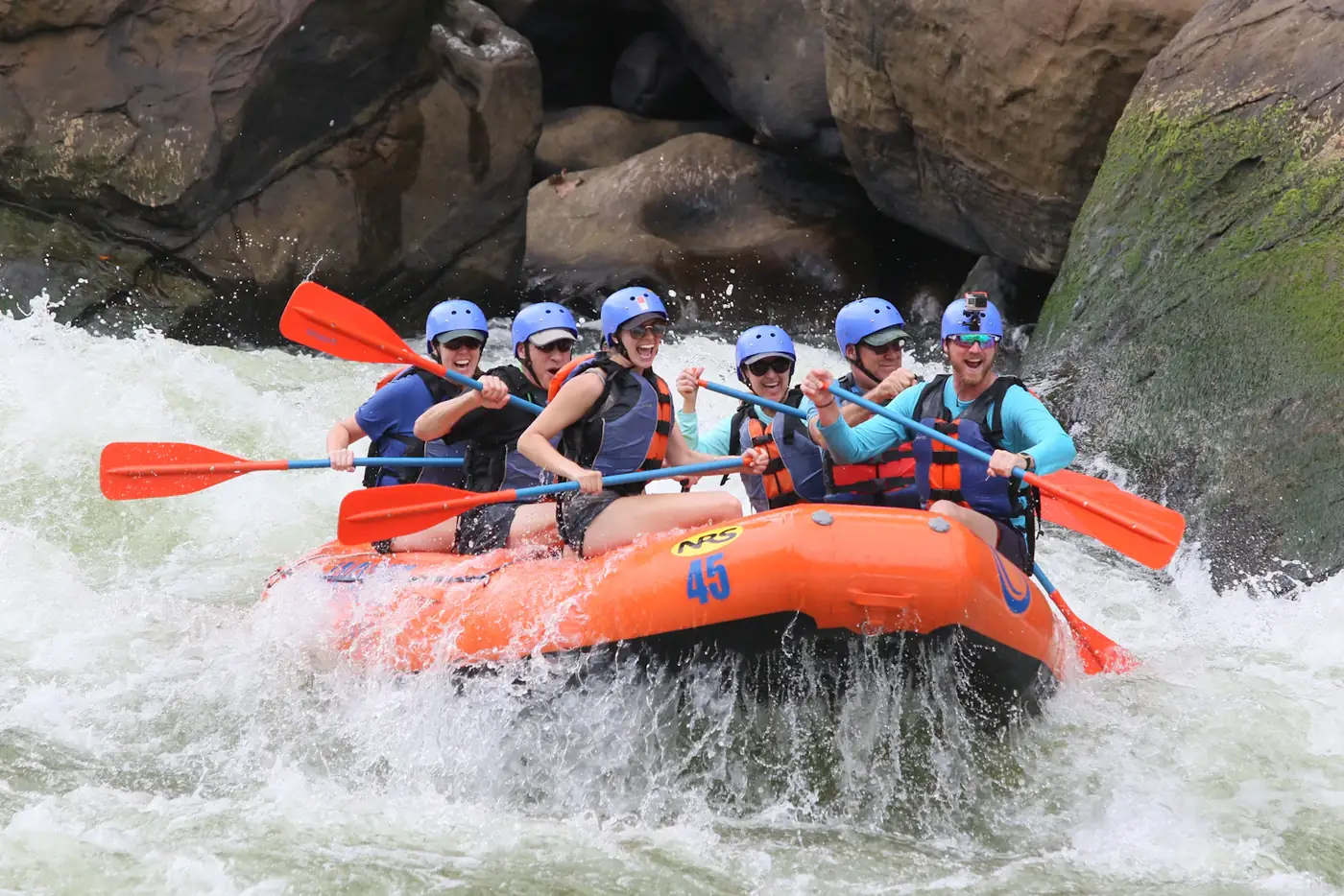A rafting team paddling an orange raft through white water